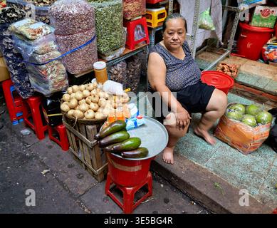 Eine Frau sitzt an ihrem Stand in Ho-Chi-Minh-Stadt und verkauft Obst und Gemüse. Der Markt ist voll und die Atmosphäre ist lebhaft. Stockfoto