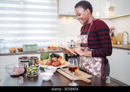 Frau, die Kochbuch liest und gesunde Mahlzeiten in der modernen Küche zubereitet Stockfoto