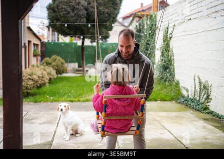 Vater-Tochter spielt auf der Schaukel mit Familienhund Stockfoto