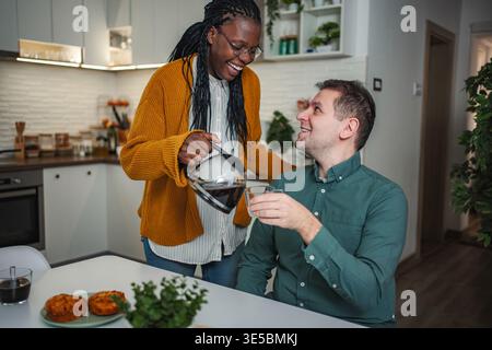 Glückliches, interrassisches Paar, das zusammen in der Küche frühstückt Stockfoto