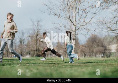 Drei Freunde laufen und spielen gemeinsam in einem Stadtpark an einem sonnigen Tag Stockfoto