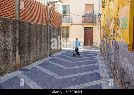 Malaga Spanien, Andalusien, El Molinillo Capuchinos Nachbarschaft, Kind Junge, der Elektroroller reitet, enge Gasse Straße städtische Wohngebäude Graffiti Stockfoto