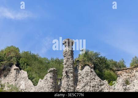 Hoher, gekappter Hoodoo in den Zone Rock Pyramiden in Lombardei, Italien, dominiert das Bild, blasse Sedimentpinnakole und gebrochene weiße Grate breiten sich unter dem Deckstein aus. Stockfoto