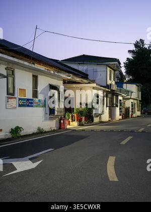 Wuhan, China - 16. Juni 2025: Asphaltierte Straße mit weißem Pfeil und gelber Fahrbahnmarkierung führt vorbei an alten zweistöckigen Wohnhäusern mit weißer Wa Stockfoto