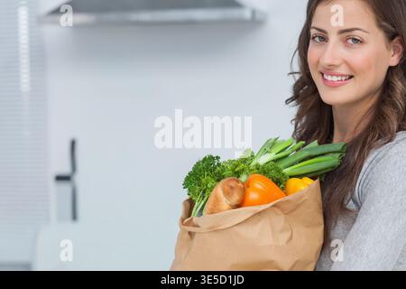 Frau, die in die Küche geht, Lebensmittelbeutel hält, animierte Etiketten, die über Lebensmitteln schweben. Gemüse, frisch, zu Hause, modern, rostfrei, Bereich Stockfoto