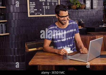 Erwachsener Mann, der an einem hölzernen Kaffeetisch auf einem Laptop unter der Tafel arbeitet, während er eine Kaffeetasse hält. Gemütlich, modern, rustikal, produktiv, freiberuflich, funktioniert Stockfoto