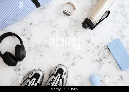 Flaches Lay-Bild mit wichtigen Fitnessgeräten auf Marmorhintergrund, mit Sneakers, einer Yogamatte, einer Wasserflasche, Kopfhörern, eine Smartwatch, ein Stockfoto