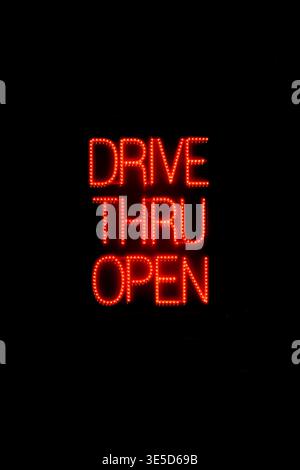 Nachts beleuchtetes Schild im Fenster eines Fast-Food-Restaurants, das die Gäste darauf hinweist, dass das Drive-Thru-Fenster geöffnet ist. Stockfoto