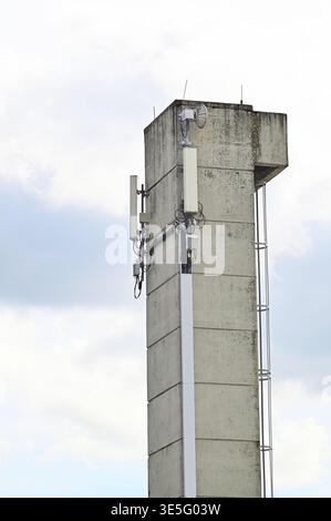 Betonturm mit Mobilfunkantennen und Kommunikationsausrüstung gegen bewölkten Himmel Stockfoto