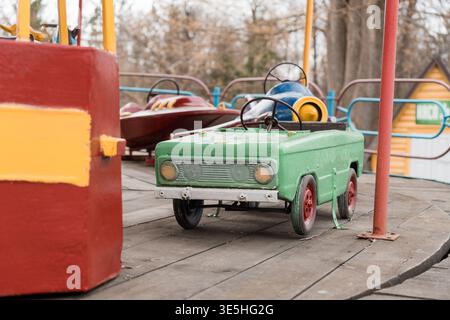 Nostalgische Szene einer alten grünen Spielzeugauto-Fahrt auf Holzplanken in der Nähe eines roten Buches in einem verblassten Vergnügungspark, der Retro-Charme weckt Stockfoto