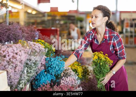 Verkäuferin mittleren Alters mit einem Strauß trockener Blumen auf dem Pflanzenmarkt Stockfoto