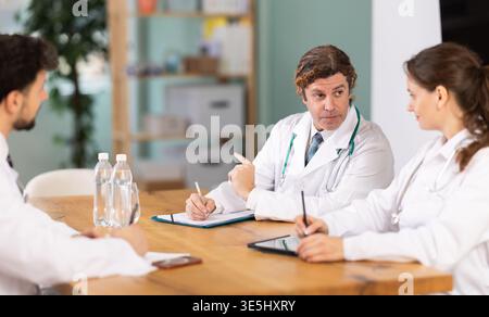 Vertreter der medizinischen Fachgemeinschaft sitzen am Tisch und plaudern Stockfoto