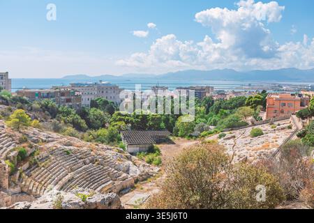 Römisches Amphitheater von Cagliari in Sardinien, Italien. Alte Steinruinen steigen hinab in einen üppig grünen Park und eine Skyline der Küstenstadt, die auf das blaue Ich trifft Stockfoto