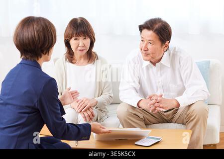 Ein japanisches Seniorenpaar diskutiert seine zukünftigen Finanzpläne mit einem Finanzplaner zu Hause Stockfoto