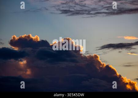 Dramatische dunkle Wolken mit leuchtenden goldenen Kanten, die lebendiges Licht bei Sonnenuntergang einfangen und einen Kontrast zu einem sanften blauen Himmel bilden Stockfoto