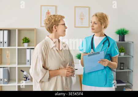 Schwester und ältere Patientin stehen während der Sprechstunde in der Klinik zusammen. Stockfoto