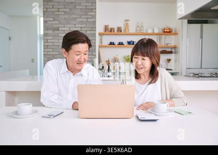 Japanisches Seniorenpaar diskutiert über das zukünftige Leben und die finanziellen Pläne auf einem Laptop zu Hause Stockfoto