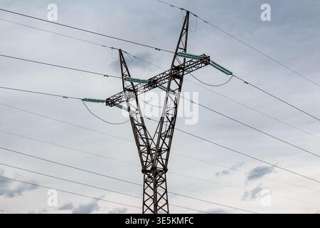 Robuster Hochspannungs-Pylon, der ein Netz von Stromleitungen gegen einen bewölkten Himmel trägt. Unverzichtbare moderne Infrastruktur Stockfoto