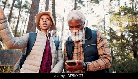 Wandern, altes Paar und verloren mit Smartphone im Wald, Gespräch und Suche nach Ort auf der Website. Outdoor, Senior Wanderer und Schwarze mit Stockfoto