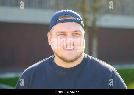 Porträt eines lächelnden jungen Mannes, der draußen im warmen Sonnenlicht eine Mütze und ein lässiges Sweatshirt trägt. Stockfoto