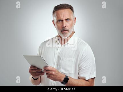 Geschäft, Mann und verwirrt mit Tablet im Studio für gefälschte Nachrichten, Plagiate und Unglauben. Raum, reifer Editor und überraschendes Porträt mit Technik Stockfoto