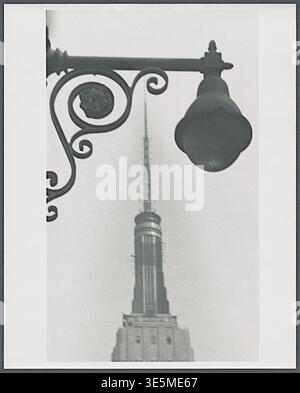 Anthony Angel (1906–1967) - Detailansicht des oberen Teils des Empire State Building durch eine kunstvolle Straßenlaterne (im Vordergrund), Manhattan, New York City, New York - 1959 Stockfoto
