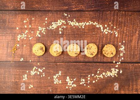 Blick von oben auf fünf Schokoladenkekse auf rustikalem Holz, eingerahmt mit Haferflocken, minimalistisches gesundes Frühstückskonzept mit starkem Kopierraum und hausgemachtem sna Stockfoto