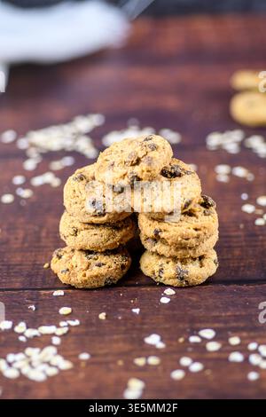 Nahaufnahme von gestapelten Schokoladenkeksen auf einem rustikalen Holztisch mit verstreuten Haferflocken und geringer Tiefe, hausgemachtes Frühstück-Snack-Konzept. Stockfoto