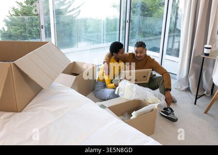 Die Kartons auspacken, verschiedene Paare sitzen im Schlafzimmer in der Nähe von Fenstern und untersuchen den Rahmen des Luftpolsterfilms Stockfoto