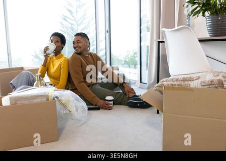 Kaffeetassen halten, verschiedene Paare sitzen auf Teppich durch Glasschiebetüren, mit Umzugskästen Stockfoto