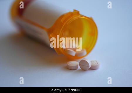 Eine orangene verschreibungspflichtige Flasche kippte um und verschüttete Pillen auf weißem Hintergrund. Makro-Seitenansicht mit Kopierraum. Gesundheitsmedizinisches Konzept. Stockfoto
