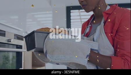 Erwachsene Frau Rothemd Schürze Fäuste ziehen Brotpfanne aus dem Ofen in der Küche goldene Sterne, Kopierraum Stockfoto