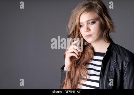 Eine Frau mit langen Haaren trägt eine schwarze Jacke und ein weiß gestreiftes Hemd. Sie blickt mit nachdenklichem Ausdruck in die Kamera Stockfoto