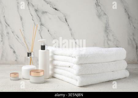 Stapel sauberer Handtücher, Kosmetikprodukte und Schilfdiffusor auf hellem Hintergrund Stockfoto