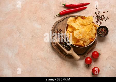 Schüssel mit köstlichen Kartoffelchips, Tomaten und Chili-Pfeffer auf rosa Grunge-Hintergrund Stockfoto