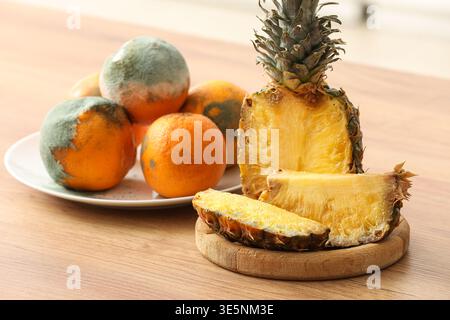 Teller mit schimmeliger Ananas und Orangen auf der Theke in der Küche Stockfoto