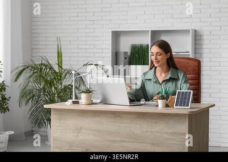 Weibliche Ingenieurin mit Laptop- und Windturbinenmodellen, die am Tisch im Büro arbeiten Stockfoto