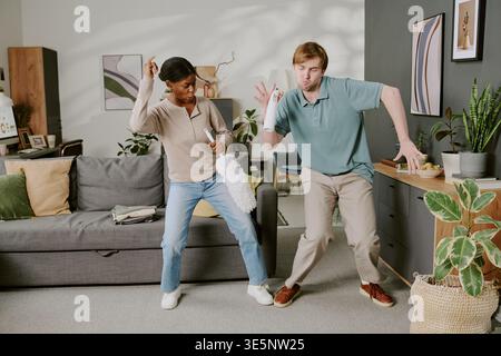 Multiethnisches Erwachsenes Paar, Das Beim Gemeinsamen Säubern Des Heims Tanzt Stockfoto