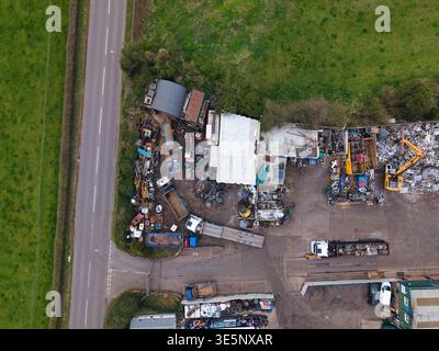 Aus der Vogelperspektive einer chaotischen Szene aus Schrott und Maschinen steht im Kontrast zu den angrenzenden üppigen grünen Feldern und der grauen Straße, Stafford, England, Stockfoto