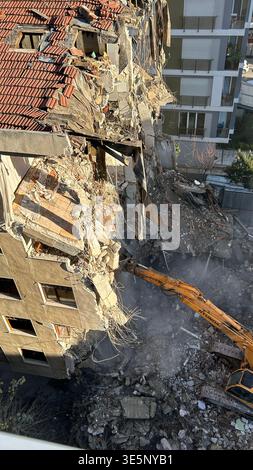 Gelber Bagger, der ein altes Wohngebäude auf einer städtischen Baustelle abriss. Eine detaillierte Ansicht von Stadterneuerung, Zerstörung und Stockfoto