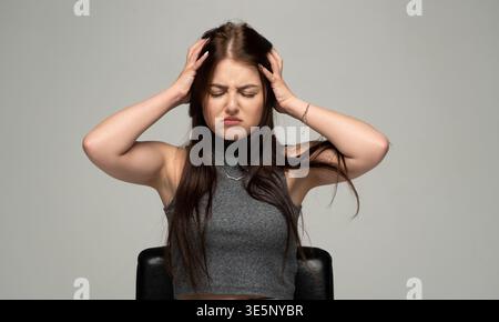 Junge Frau, die an Kopfschmerzen oder Migräne leidet, frustriert und gestresst ist und Hände an Kopf hält Stockfoto