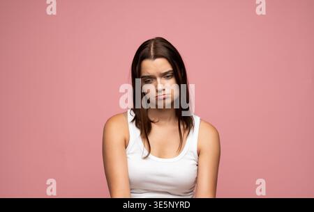 Junge Frau, die traurig und niedergeschlagen ist, melancholisch oder depressiv ist und sich auf rosa Hintergrund posiert Stockfoto