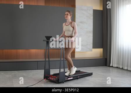 Junge Frau, die zügig auf einem Faltband in einem modernen Wohnraum spaziert und täglich Cardio für Fitness, Wellness und gesund übt Stockfoto