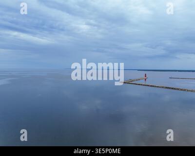 Aus der Vogelperspektive eines einsamen roten Leuchtturms, der am Hafeneingang Wache steht, spiegelt sich in den ruhigen, weitläufigen Gewässern des Lake Michigan wider Stockfoto