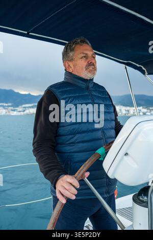 Reifer Mann, der das Segelboot auf der Ozeanreise steuert Stockfoto