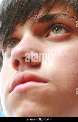 Nahaufnahme eines jungen Mannes mit braunem Haar und grünen Augen. Er hat einen nachdenklichen, ehrgeizigen Ausdruck, wenn er zublickt Stockfoto