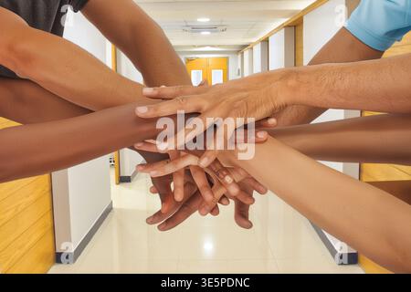 Eine Nahaufnahme multirassischer Hände, die in einem hellen, modernen Büro- oder Krankenhausflur zusammengestapelt sind und Teamwork, Inklusion und Corporate Solida symbolisieren Stockfoto
