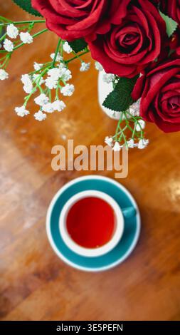 Teal Tasse mit rotem Tee und Rosen auf Holztisch. Stockfoto