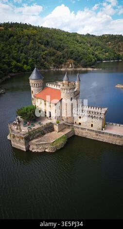 Aus der Vogelperspektive die Château de la Roche, die majestätisch auf ihrer Insel steht, eine mittelalterliche Festung, die sich im dunklen Wasser spiegelt, Saint-Priest-la-Roche, A Stockfoto