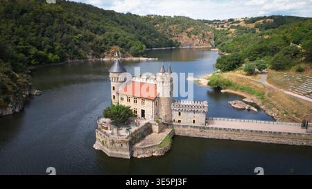 Blick aus der Vogelperspektive auf die Château de la Roche, majestätisch im glitzernden Wasser, umgeben von üppigen grünen Hügeln, Saint-Priest-la-Roche, Auvergne- Stockfoto
